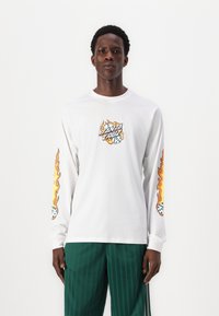 White long-sleeve t-shirt with graphic print featuring flames and dice on the front and sleeves. Paired with green striped pants.