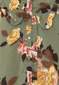 Camicia floreale in tessuto verde con rose gialle e rosa, colletto arricciato e bottoni argentati lungo la patta anteriore.