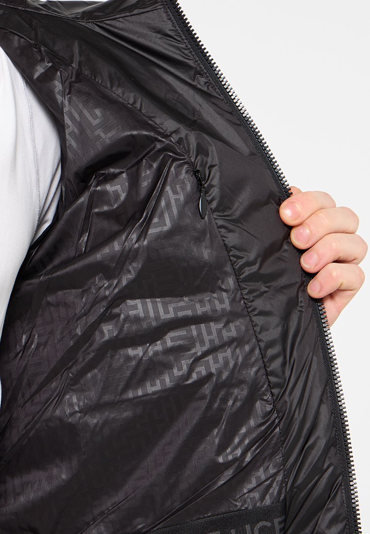 Schwarze, isolierte Weste mit einer glatten, glänzenden Außenseite, einer inneren Reißverschlusstasche und einem subtilen geometrischen Muster. Das weiche Futter erhöht den Tragekomfort.