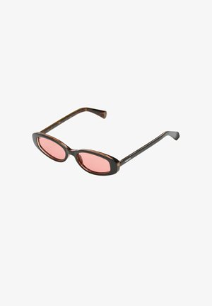 Lunettes de soleil ovales fines en écaille de tortue avec des verres teintés rose et des branches noires fines, inclinées sur fond blanc.