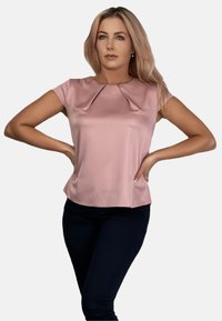Różowa satynowa bluzka z krótkim rękawem, plisowany dekolt, gładka tekstura i zaokrąglony dół, w zestawieniu z ciemnymi dopasowanymi spodniami.