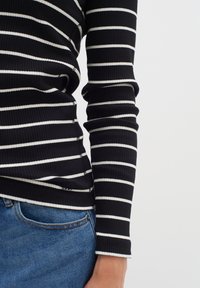 Svart- och vitt randig ribbad topp med långa ärmar, med en figurnära design och kontrasterande vit sömnad, matchad med blå denim.