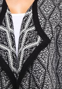 Svart och vit mönstrad cardigan med sjalkrage, prydd med diamantsformer och texturerat stickat tyg. Accentuerad med svart kant.