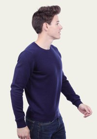 Pull en maille bleu marine avec un col rond, des manches longues et des poignets côtelés. Porté sur un jean en denim, montrant une silhouette ajustée.