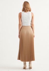 Fald med veck, högt midjeskärp i beige, tillverkad av ett slätt material, ihopparad med en ribbad vit linne och nude ankelskor.