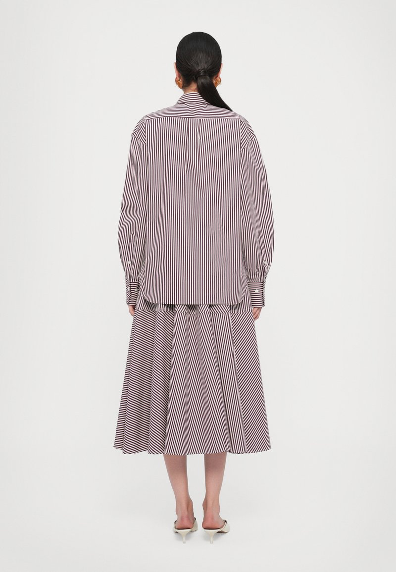 Completo maglietta e gonna a righe in rosso e bianco, con una camicia con colletto a maniche lunghe e una gonna midi svasata con pieghe.