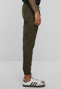 Olijfgroene tapered joggerpants met een elastische tailleband en enkelmanchetten, voorzien van zijvakjes en een zacht, geprofileerd materiaal.