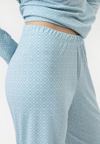 Lichtblauw pyjama set met een geometrisch wit patroon; zachte stof, elastische tailleband, lange mouwen en een ontspannen pasvorm.