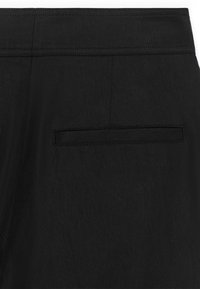 Pantalon noir à texture lisse, avec une seule poche arrière et des détails de couture subtils pour un design amélioré.