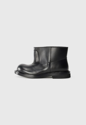 Schwarze Lederstiefeletten mit runder Schuhspitze, minimalen Nahtdetails und einer flachen Gummisohle. Glatte Textur und elegantes Design.