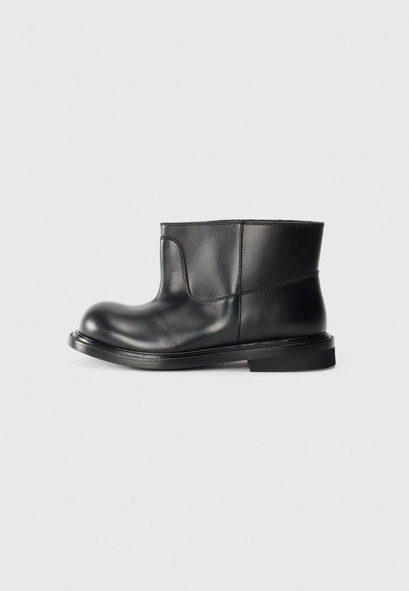 Botas de tobillo de cuero negro con punta redonda, detalles de costura mínimos y suela de goma plana. Textura suave y diseño elegante.