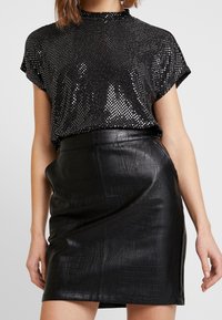 Top nero con paillettes e maniche corte abbinato a una gonna nera alta in vita in ecopelle con texture coccodrillo e zip laterale.