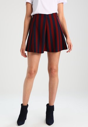 Femme portant une jupe rayée verticale taille haute bleu marine et rouge et une chemise blanche à manches courtes, associées à des bottines noires.