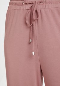 Růžové jogger kalhoty se strukturou, s elastickým páskem a šňůrkou. Stříbrné kovové detaily na koncích šňůrky. Měkká, pohodlná tkanina.