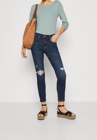 Niebieskie rurki z przetarciami, zestawione z jasnoniebieską dopasowaną bluzką i czarnymi sandałami na koturnie z plecioną podeszwą. Brązowa zamszowa torebka na ramię.