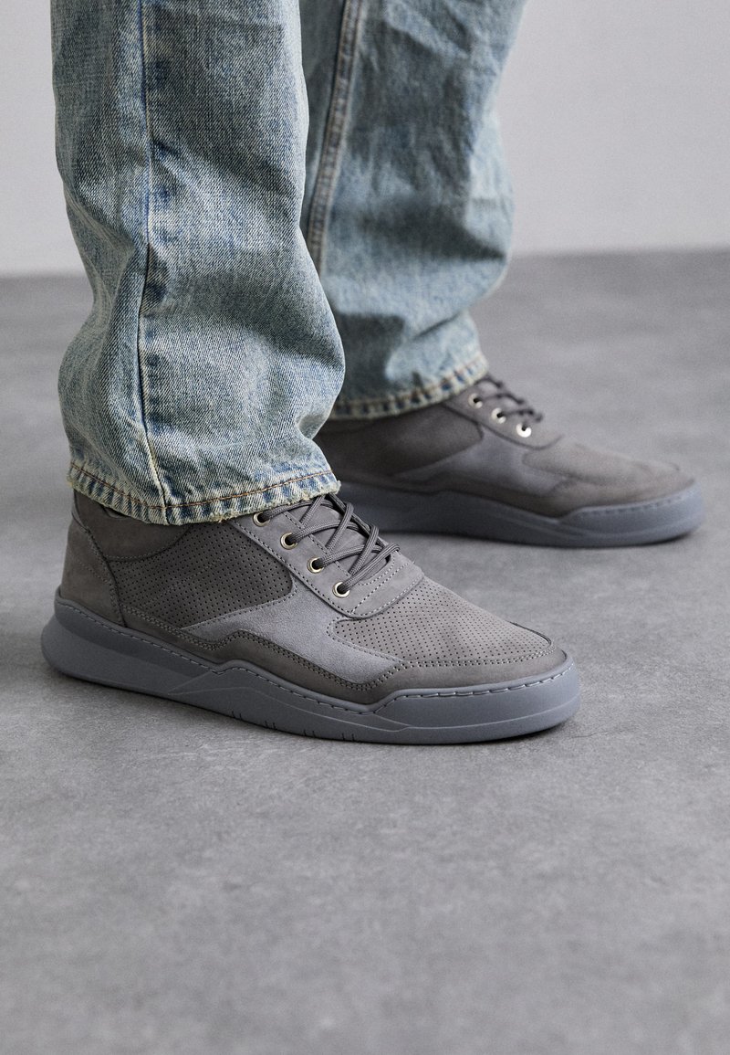 Baskets grises avec un mélange de textures lisses et perforées. Bout arrondi, semelle en caoutchouc grise et œillets en métal pour les lacets. Portées avec un jean bleu clair.