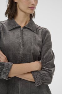 Abito camicia grigio in corduroy con zip e colletto, caratterizzato da ribbature verticali, maniche lunghe e polsini arricciati. Attento ai dettagli e dalla texture ricercata.