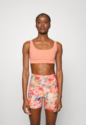 O top desportivo cropped pêssego e os calções em padrão floral apresentam um design ajustado. O tecido é suave, com cores brilhantes misturadas e uma cintura alta.