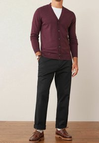 Cardigan bordeaux avec col en V, boutonné sur le devant, et manches longues, accompagné d'un pantalon noir et de chaussures marron, posé sur une surface en bois.