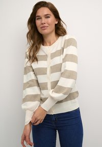 Beige and white striped cardigan with buttons, ribbed cuffs, and soft texture. Paired with blue jeans, showcasing a relaxed fit.