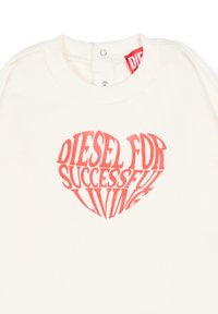 Kremowy t-shirt z czerwonym nadrukiem serca i napisem "DIESEL FOR SUCCESSFUL LIVING." Zapięcia na zatrzaski przy kołnierzyku.