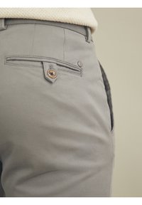 Lähikuva harmaista housuista, joissa on napitettava takatasku, ja beiget neulotut villapusero näkyy osittain vyötärön yläpuolella.