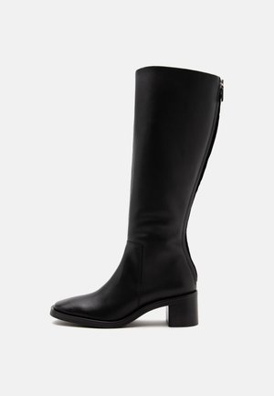 Botte haute en cuir noir avec un petit talon carré et une fermeture éclair à l'arrière, vue de côté sur fond blanc.