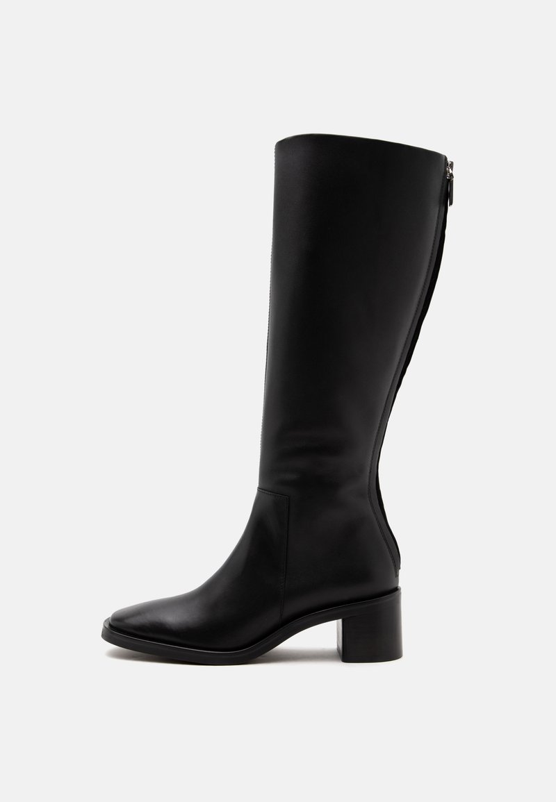 Botte haute en cuir noir avec un petit talon carré et une fermeture éclair à l'arrière, vue de côté sur fond blanc.