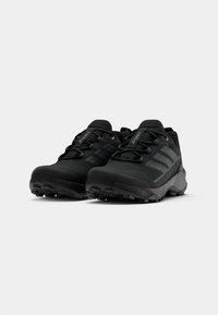 Schwarze Sportschuhe mit strukturiertem Obermaterial, ausgestattet mit einer Schnürung und einer Gummisohle mit hervorgehobenem Profil für besseren Halt. Drei Streifen an den Seiten.