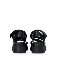 Black platform sandals featuring a layered design, smooth leather straps, and a textured sole. Adjustable ankle straps enhance fit.