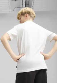 Camiseta blanca de manga corta hecha de una tela suave, con un ajuste relajado y un dobladillo recto. La vista posterior muestra un diseño simple y costuras mínimas.