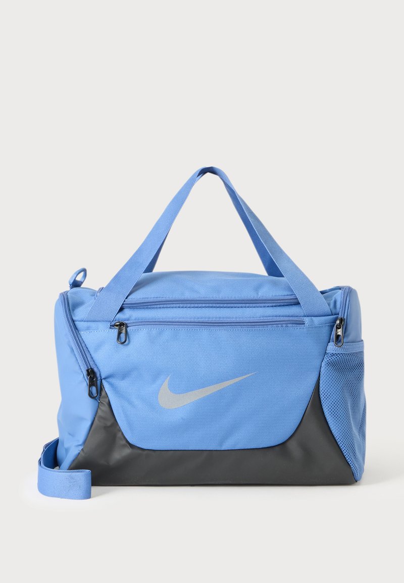 Μπλε και μαύρη αθλητική τσάντα Nike με φερμουάρ, διπλές λαβές και πλαϊνή τσέπη από διχτυωτό υλικό σε απλό ανοιχτό φόντο.
