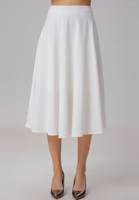 Jupe midi évasée blanche en tissu léger, avec une texture lisse et une taille ajustée, associée à des chaussures à talons hauts brillantes.