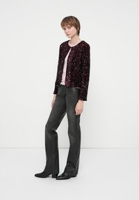 Burgundi spalvos blizgučių švarkas su apvaliu iškirpimu, vilkimas ant šviesiai rožinės palaidinės, derinamas su juodomis plačiomis kelnėmis ir juodais smailiais batais.