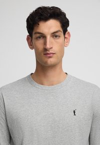 Szara koszulka z długim rękawem wykonana z miękkiej bawełny, z okrągłym dekoltem i małym czarnym logo golfisty na lewej piersi. Gładka struktura.