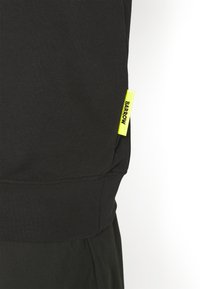 Vêtement en tissu noir avec une étiquette jaune vif portant la mention « BARROW » cousue près de la couture.