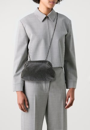 Borsa a rete metallica con una forma curva, caratterizzata da una combinazione di colori nero e argento e una tracolla a catena. Indossata sopra un abbigliamento a quadri.