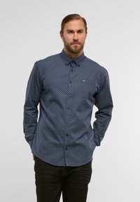 Navy-Button-Up-Hemd mit kleinem geometrischen Muster, klassischem Kragen und langen Ärmeln, kombiniert mit dunklen Hosen.