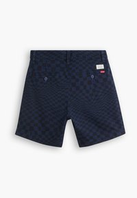 Merkit, joissa on musta ruutukuvio, kaksi takataskua, nappikiinnitys ja vyötäröllä oleva merkki.