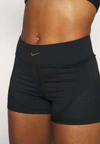 Shorts de sport noirs avec une taille haute, présentant un petit logo Nike gris et une texture côtelée sur les côtés. Fabriqués à partir d'un matériau extensible.
