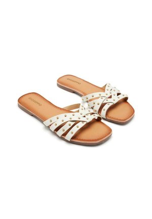 Sandalias planas blancas con múltiples correas cruzadas, decoradas con tachuelas doradas. Plantillas y suela en tono bronceado, con un diseño de punta cuadrada.