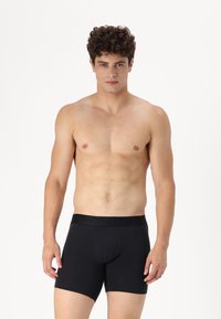 Schwarze Boxershorts aus weichem elastischem Bund, mit enger Passform und glatter Textur. Vorderer Taschenbereich für Unterstützung und Formgebung.