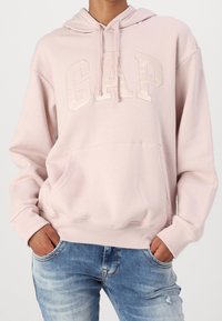 Sudadera rosa claro hecha de una tela suave, con un bolsillo frontal, puños acanalados y el logo "GAP" en un diseño en relieve.