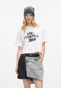 Balta trumpa marškinėliai su juodu „KARL LAGERFELD JEANS“ grafiku, derinami su juodai ir pilkai pataisyta džinsine sijonu, turinčiu pabirusias kraštines.