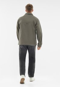 Zielona oliwkowa koszula z kołnierzykiem, długimi rękawami, zapinanymi mankietami i prostym krojem, zestawiona z ciemnym dżinsami i białymi trampkami.