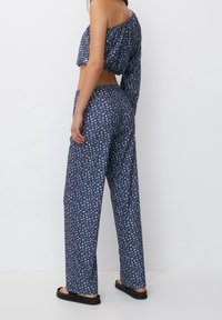 Marineblaue Zweiteiler bestehend aus einem einseitig tragebaren Cropped-Top und weiten Hosen, beide mit floralem Muster und aus leichtem Stoff.