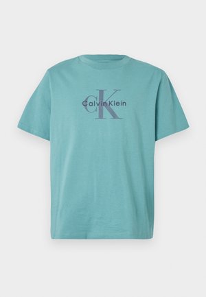 Tirkizna pamučna majica s natpisom "Calvin Klein" i oznakom "cK" u tamnosivoj boji na sredini. Standardni okrugli izrez i kratki rukavi.