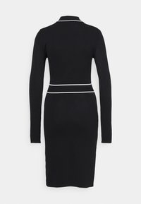 Robe noire cintrée à manches longues avec des bordures blanches au col et à la taille, présentée de dos sur un fond clair uni.