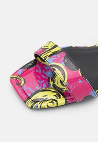 Sandale slide à bout ouvert avec un motif abstrait coloré en jaune, rose, bleu et noir, avec une seule large bride sur le pied.