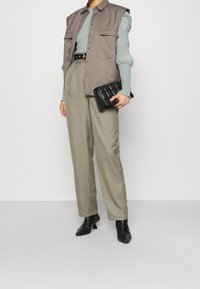 Šedá bezrukávová vesta přes světle zelený svetr, doplněná béžovými kalhotami s vysokým pasem a černými kotníkovými botami. Kabelek je černý, prošívaný.